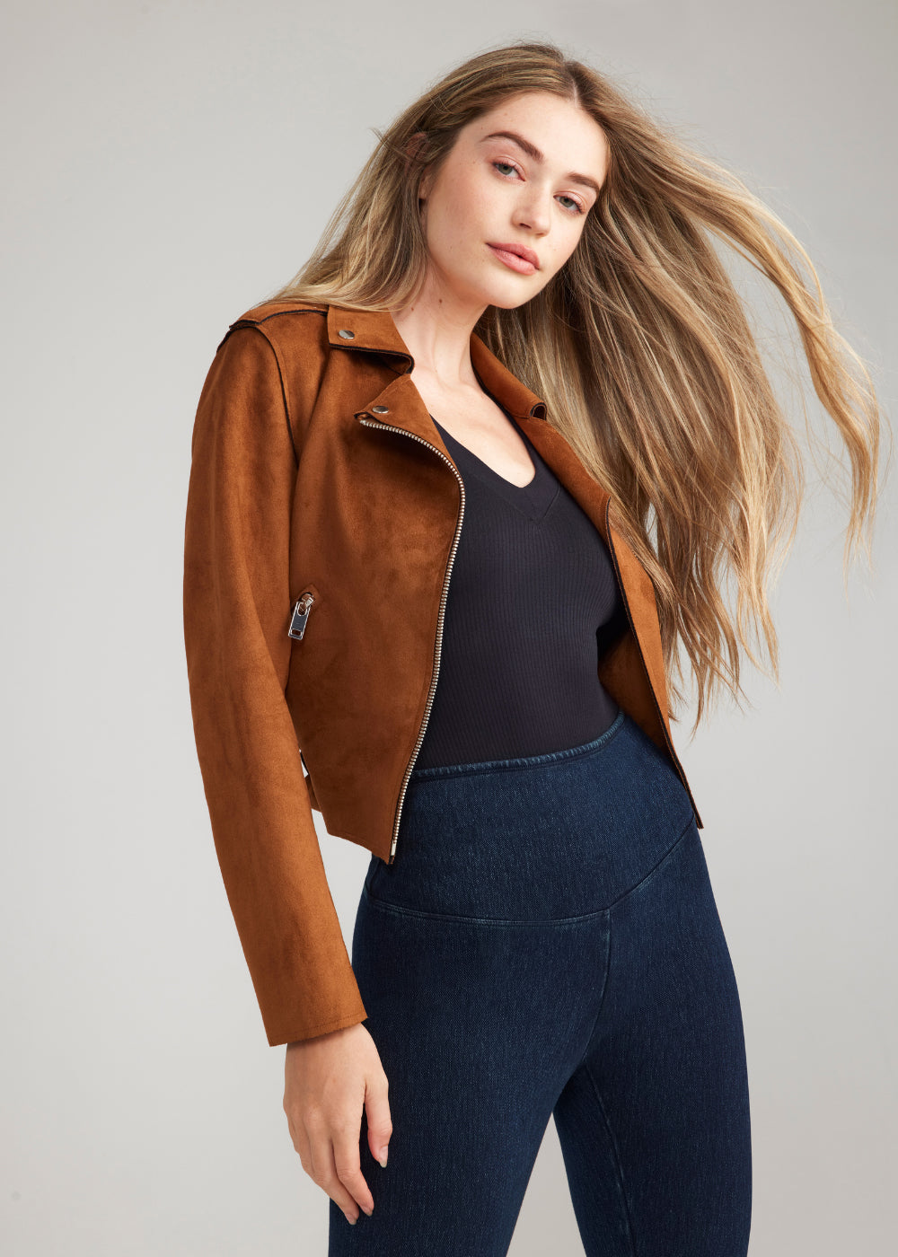 hailey v-neck thong bodysuit - rib seamless in Black, denim bootcut shaping legging in True Indigo and a suede jacket in tan worn by a woman standing slightly to the side Yummie