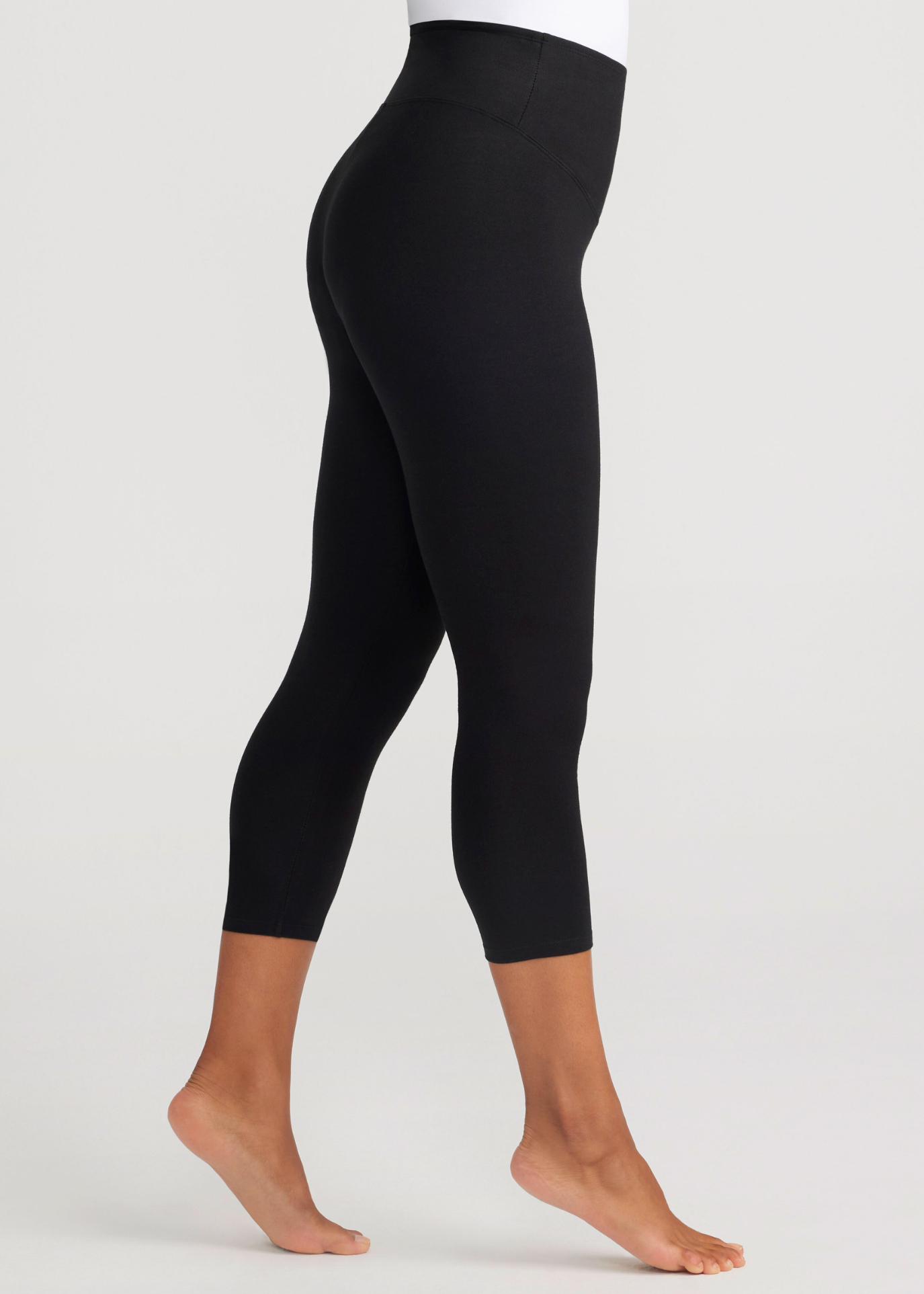 gloria 7/8 ankle shaping legging - cotton stretch in black worn by a woman standing sidways with her right foot in front of her on her toes Yummie