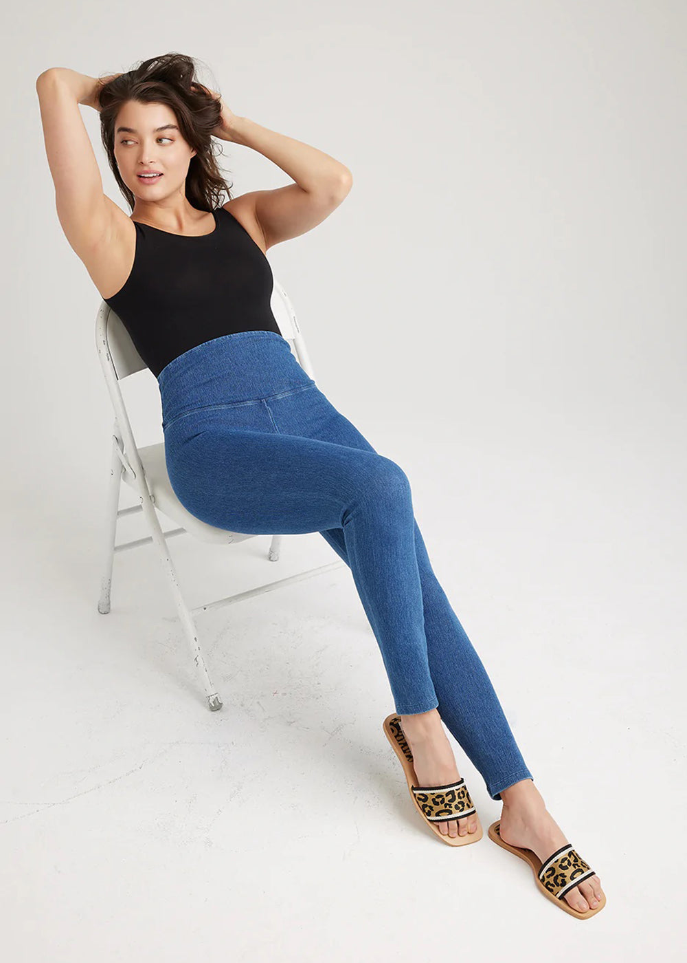 denim shaping legging in Mid Wash and ruby shaping full back bodysuit - cotton seamless in Black worn by a model reclining in a chair with hands in hair Yummie