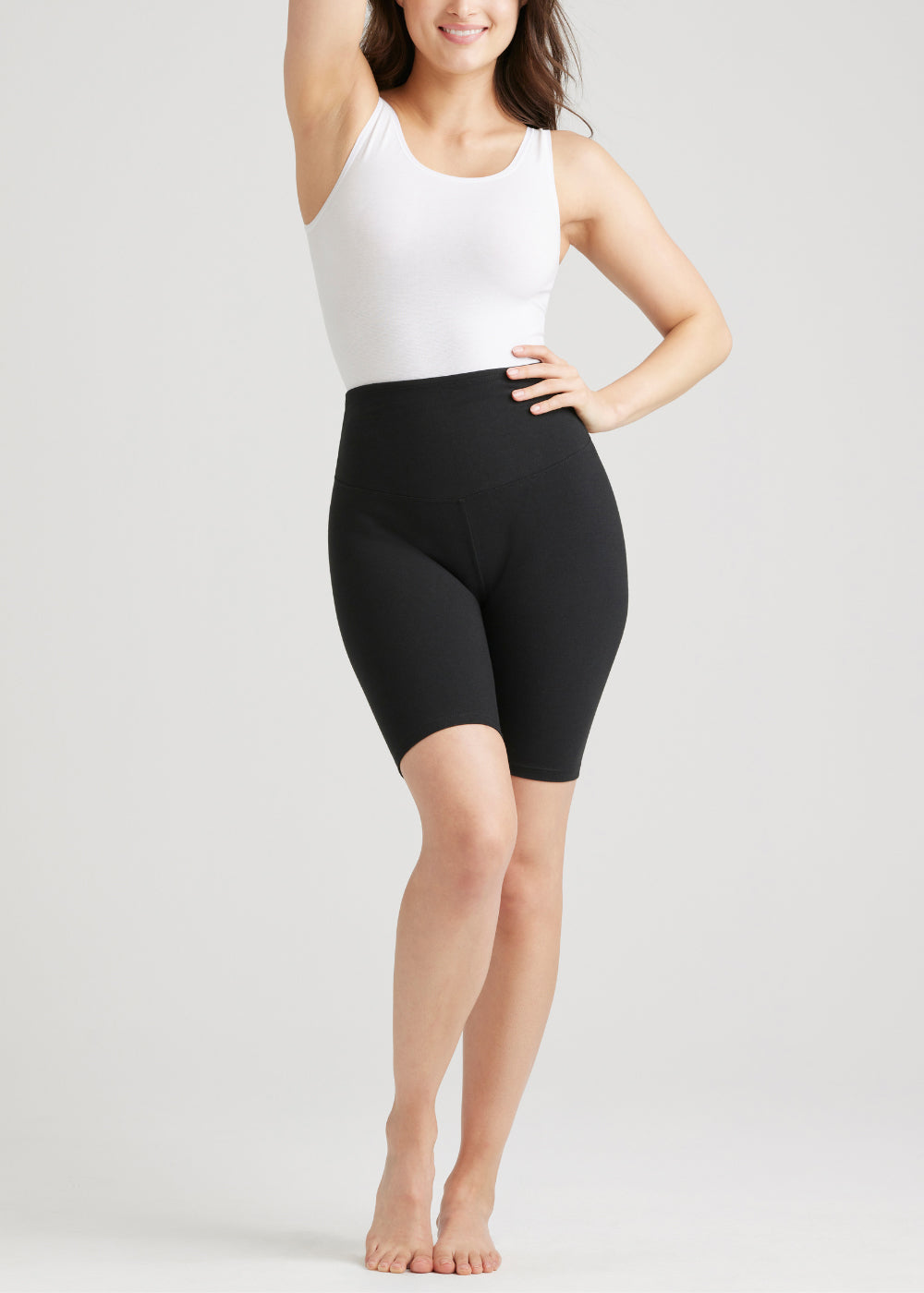 mel shaping biker short - cotton stretch in Black and  ruby shaping full back bodysuit - cotton seamless in White worn by a woman standing facing forward with one hand at waist and the other arm raised overhead Yummie