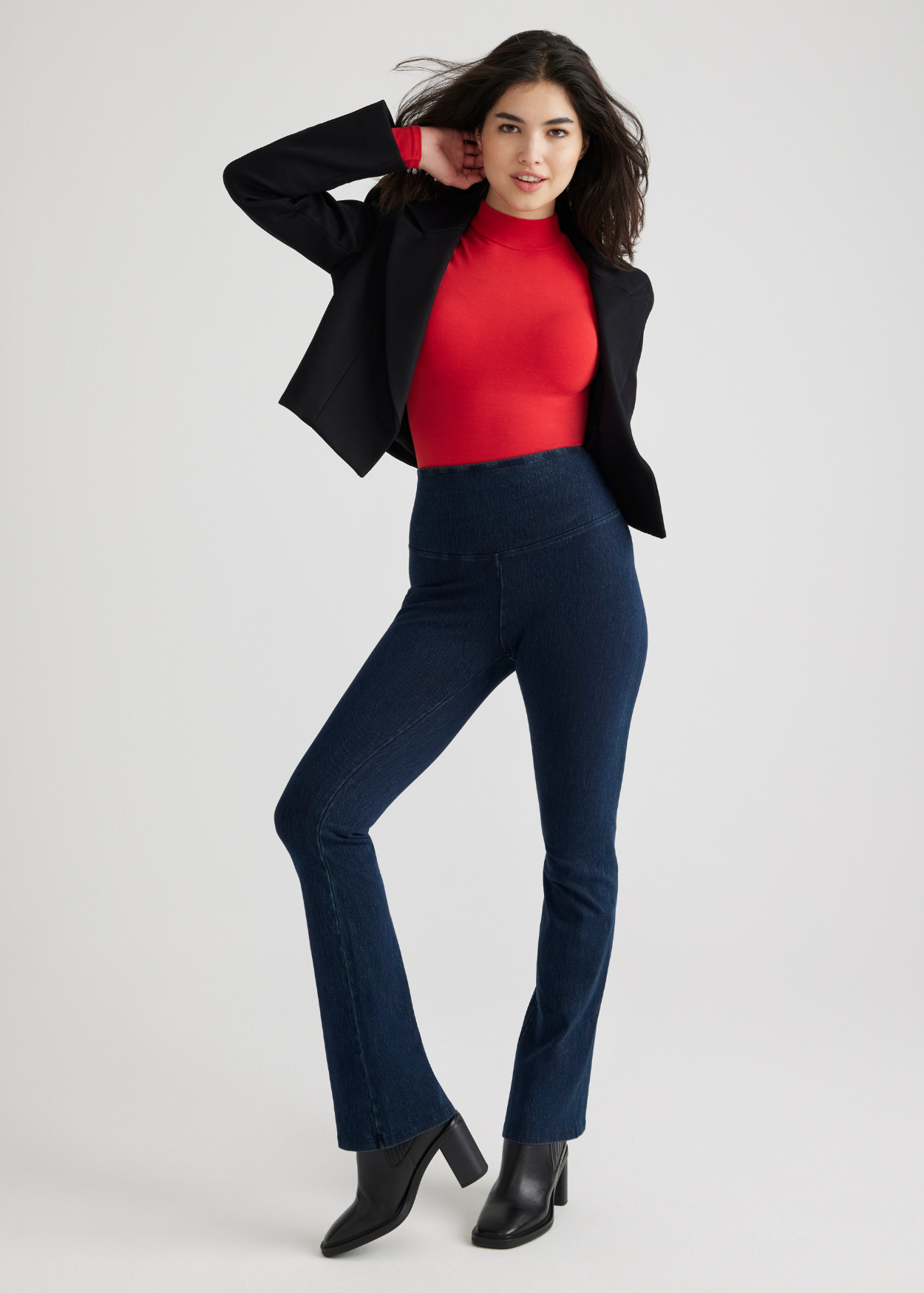 madelyn mock neck long sleeve shaping bodysuit - outlast® seamless in Salsa,  denim bootcut shaping legging in True Indigo and a black blazer worn by a woman standing facing forward with one hand at neck and the other behind her back Yummie