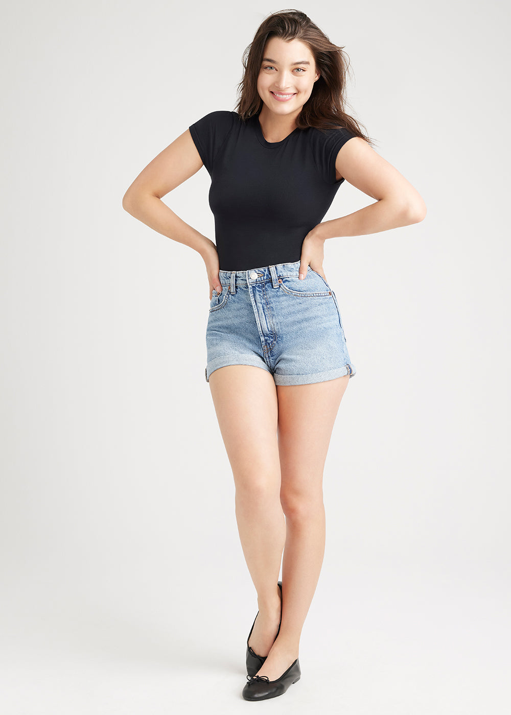 short sleeve shaping thong bodysuit - outlast® seamless in Black and jean cutoff  shorts worn by a woman  standing facing forward with hands on waist Yummie