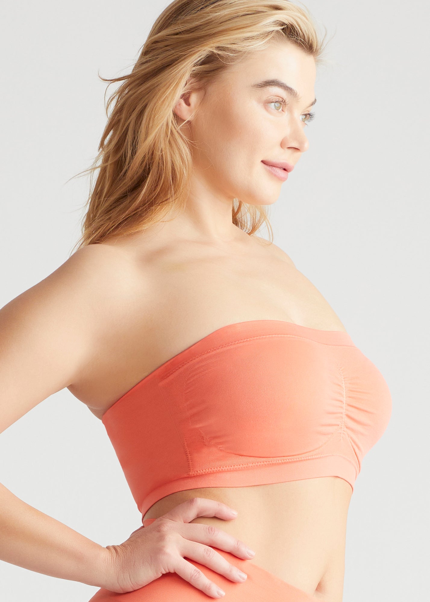 bandeau bra - seamless in Peach Echo worn by a woman standing sideways with right hand on hip Yummie