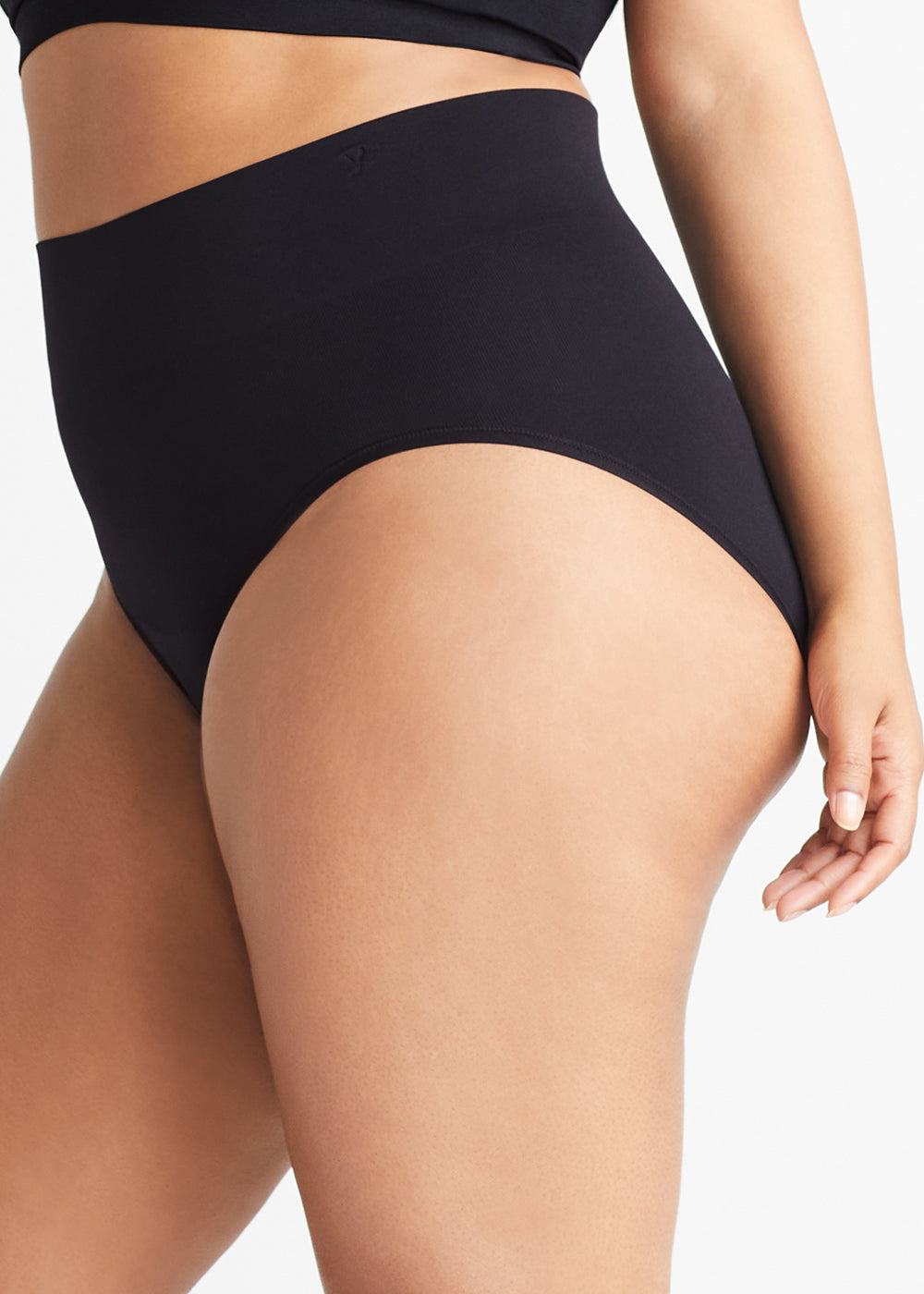 livi comfortably curved smoothing brief - seamless in Black worn by a woman standing sideways with left arm at side Yummie