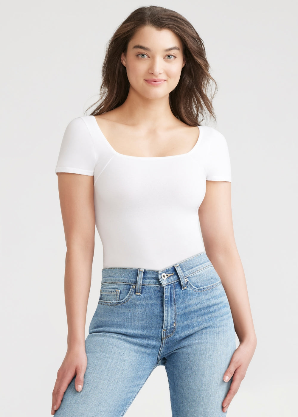 anette shaping thong bodysuit - cotton seamless in White and jeans worn by a woman standing facing forward with hands on sides of thighs Yummie