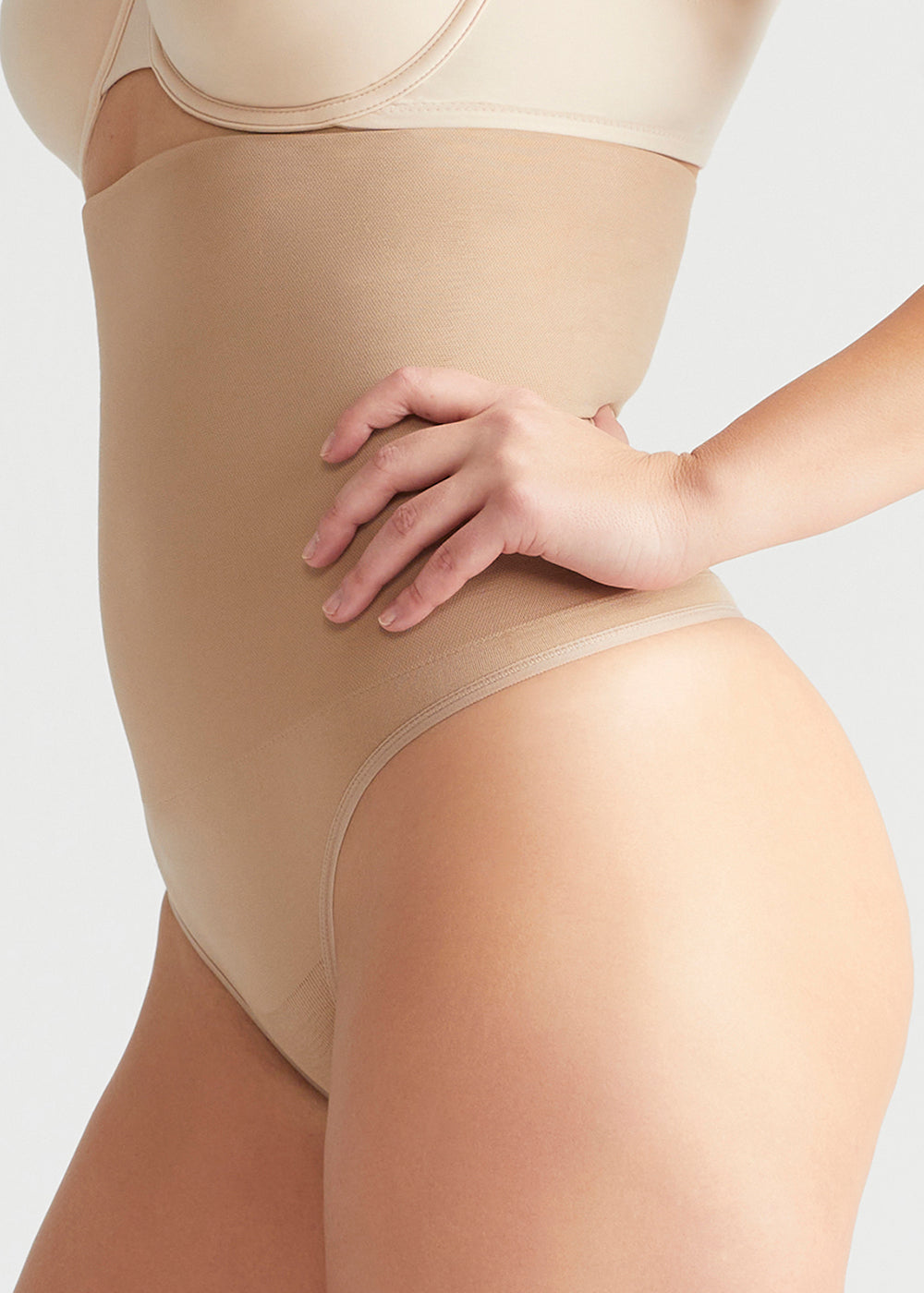 seamless solutions - high waist shaping thong in Almond worn by a woman standing sideways with hand at waist Yummie