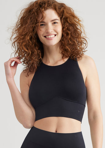 kelly high-neck longline bra top - seamless in black worn by a woman standing facing forward with her right arm bent touching her hair Yummie