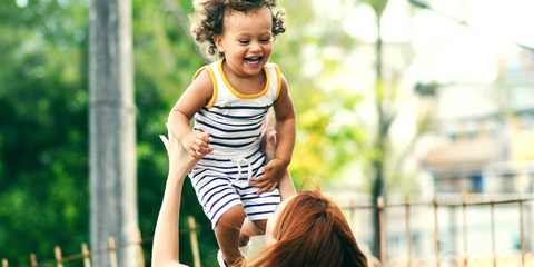 Parent playfully tossing smiling toddler into the air