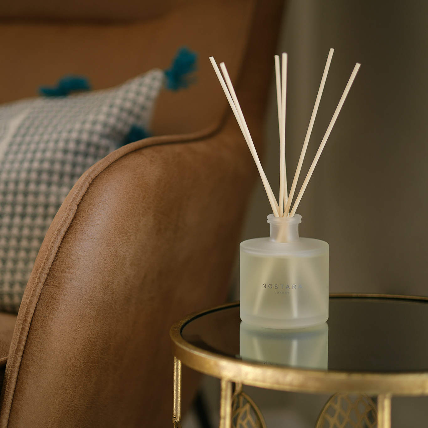 Nostara scented reed diffuser on glass table next to leather chair