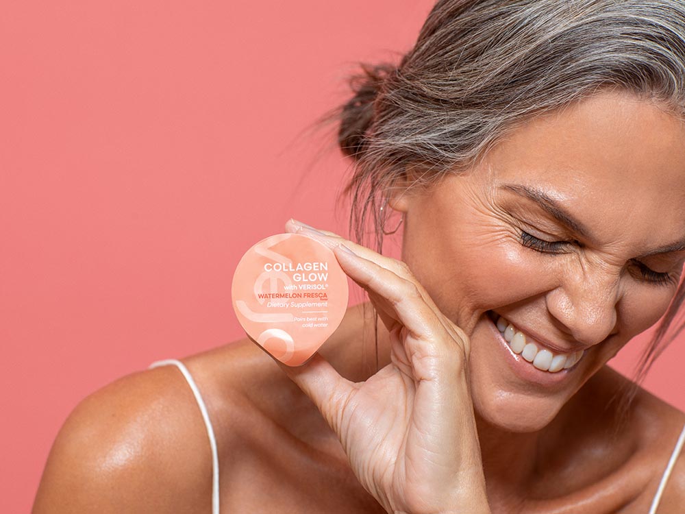 A close up of Vejo's Collagen Glow blend held by a woman laughing in front of a pink background.