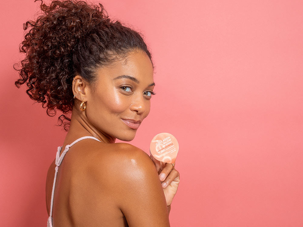 A close up of a woman holding Vejo's Collagen Glow pod standing in front of a pink backdrop.