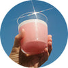 A hand holding a Vejo Collagen Glow smoothie against a deep blue sky.