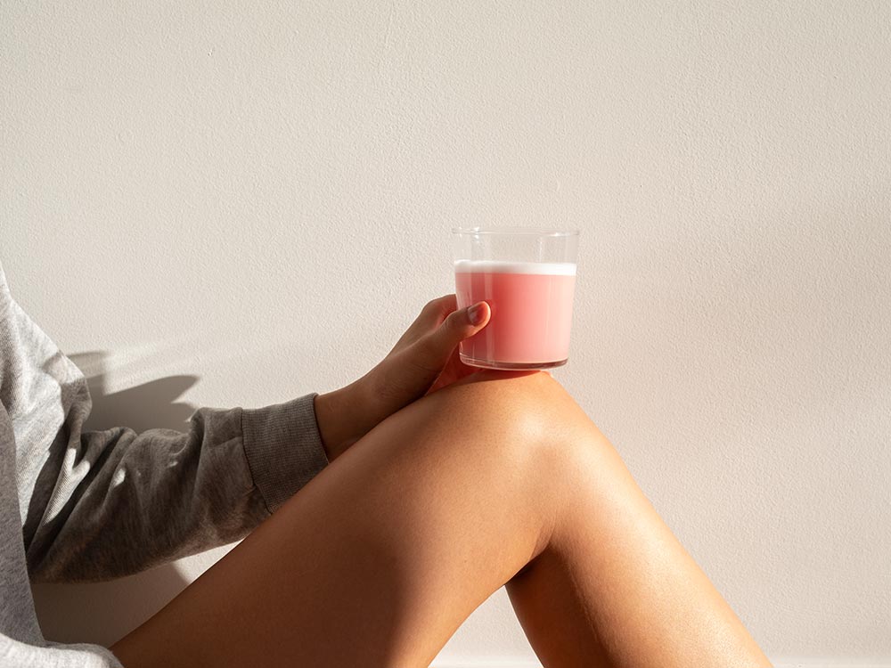 The morning sun hitting a blended smoothie of Vejo's Collagen Glow, resting comfortably on top of a woman's leg.