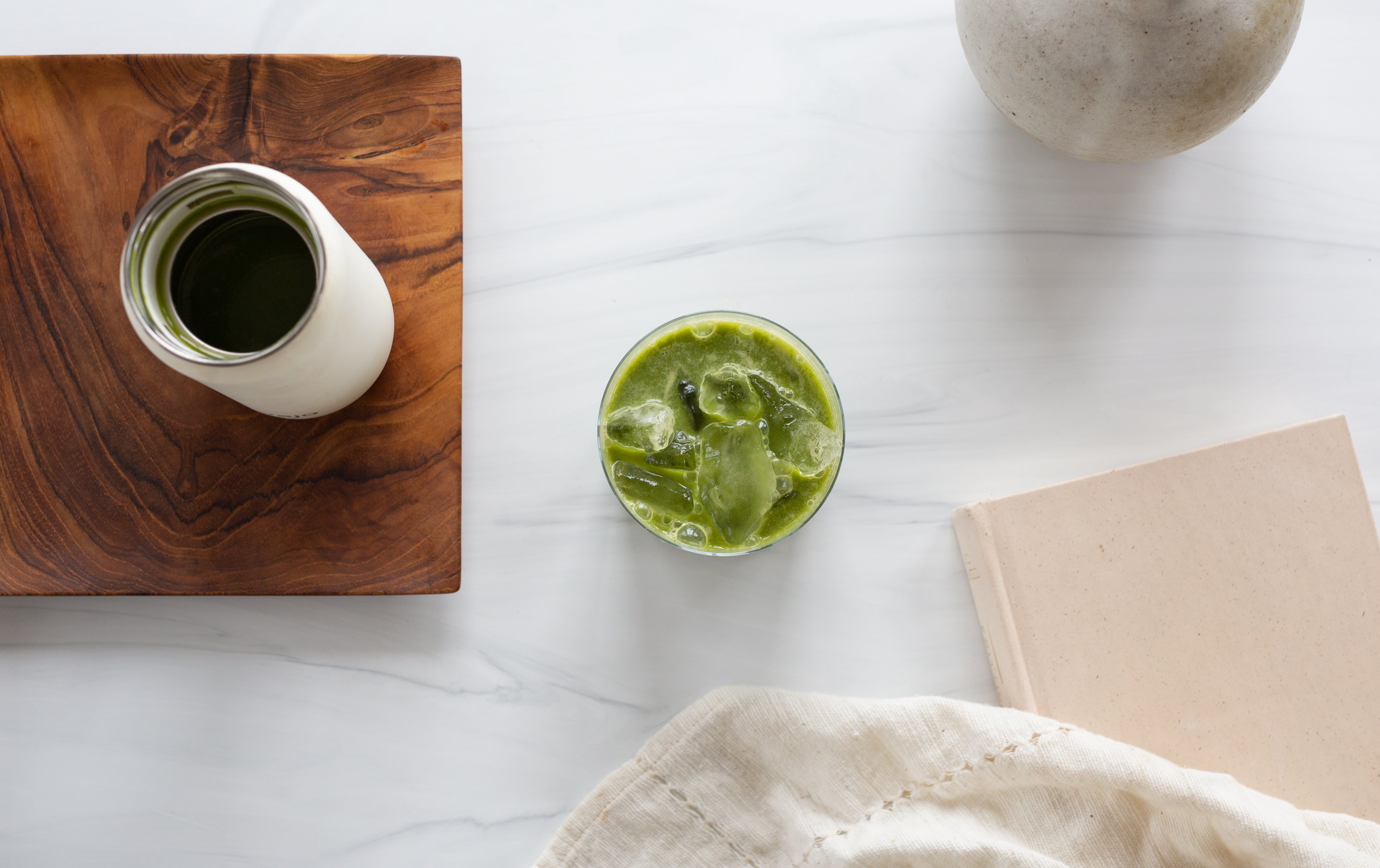 Vejo's new Matcha Latte blend photographed from overhead sitting in a glass cup with ice on a white marble countertop and kitchen towel tucked to the side of a white Vejo device.
