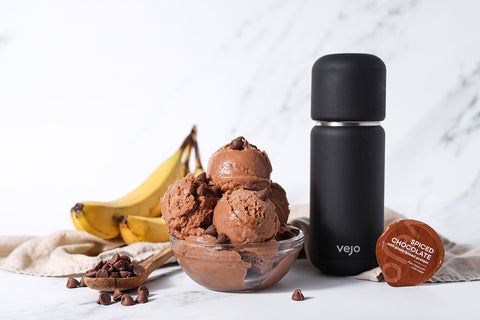 A bowl of chocolate nice cream beside a brown spiced chocolate Vejo blend and black Vejo blender.