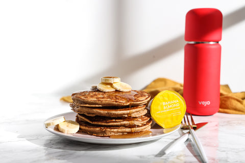 A stack of savory banana pancakes beside a yellow banana almond Vejo blend and red Vejo blender.