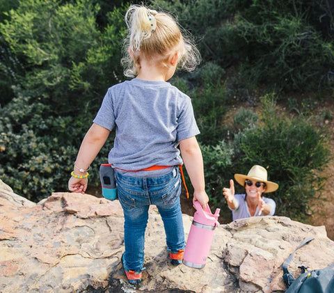 A mom reaching for her young daughter holding a pink Rambler Jr. while climbing down a hill