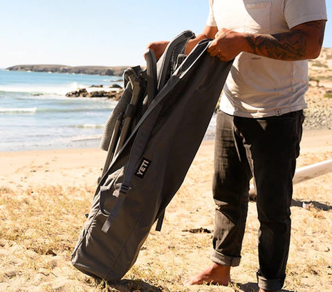 a man pulling out a  Yeti Trailhead Camp Chair in a bag beside the beach