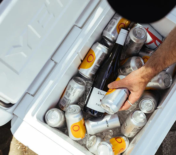 a white YETI Tundra® 65 Cool Box filled with variety of canned drinks and a bottled of wine