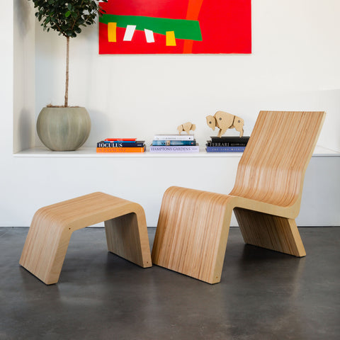 image of a modern lounge chair and ottoman in front of a modern red painting.  there are books and a wooden bison sculpture on the shelf behind the chair.