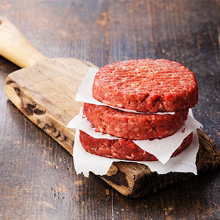 Three raw hamburger patties stacked on a wooden cutting board.