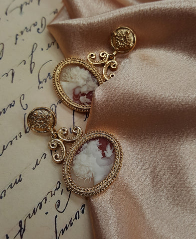 A pair of vintage earrings with gold frames and white cameos lying on an old letter