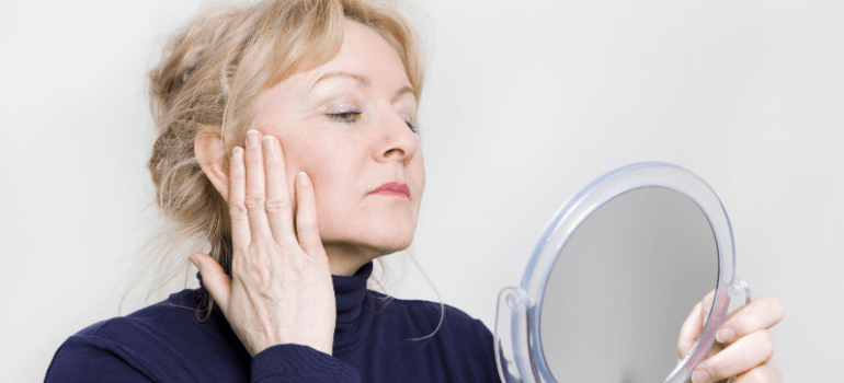 middle-aged woman looking at skin in the mirror