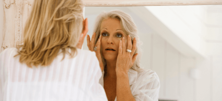 woman looking at skin in the mirror