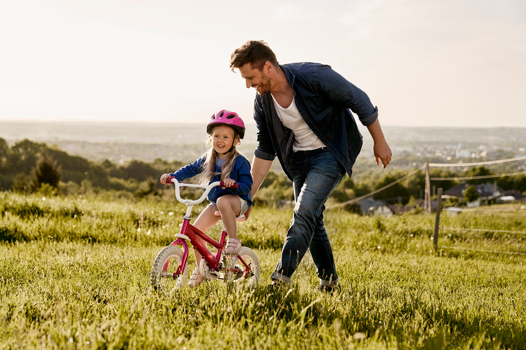 A father helping his daughter ride a bike outside.