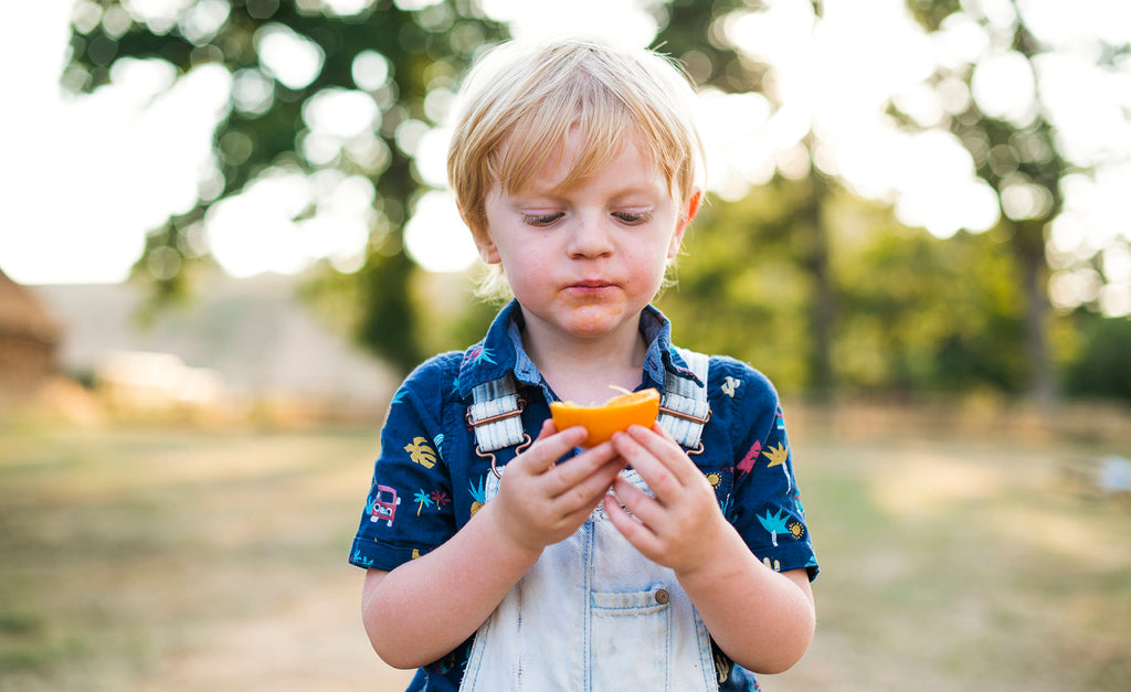 A boy eating an orange while outside.