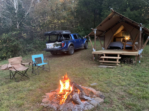 Platform canvas glamping tent beside fire pit and camping chairs.
