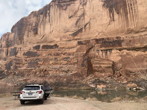 White car parked beside large red rock face at a campground near Arches National Park.