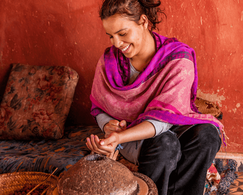 Eine sitzende und lachende marokkanische Frau bei der Herstellung von Arganöl.
