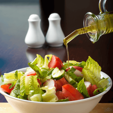 Eine großer Schüssel mit buntem Salat. Es wird ein Salatdressing mit Leinöl darüber gegossen.