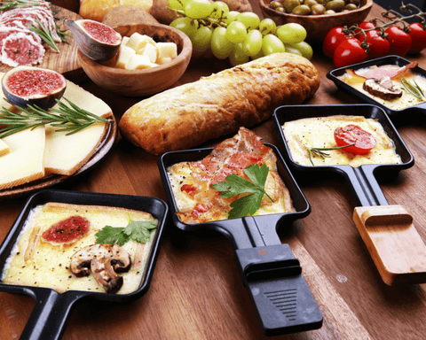 Raclette Pfännchen mit Wurst und Käse überbacken auf einem Tisch dekorativ angerichtet.