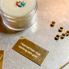 Workbench with raw gold sheet, tubes and a container with five loose gemstones