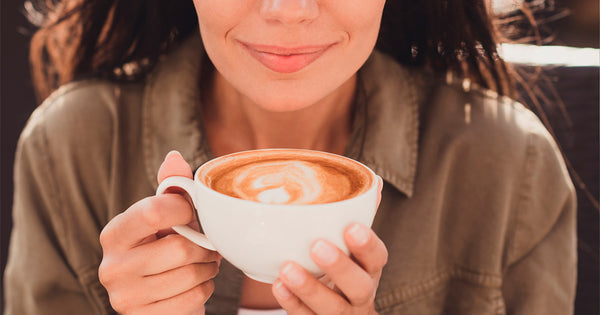 Pessoa segurando uma xícara de café com as mãos enquanto mostra um leve sorriso.