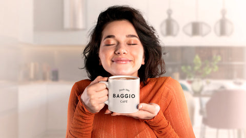 Pessoa vestindo uma blusa laranja e segurando uma caneca de café Baggio com as duas mãos enquanto sente o aroma de olhos fechados.