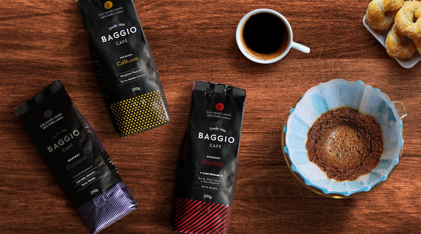 Pacotes de café Baggio colocados em uma mesa de madeira com uma xícara e um coador de café ao lado.