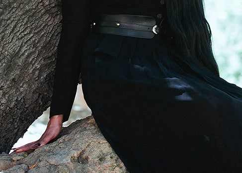 Detail image of the arm and skirt of a black vintage Sue Wong dress, and a corset belt over it.