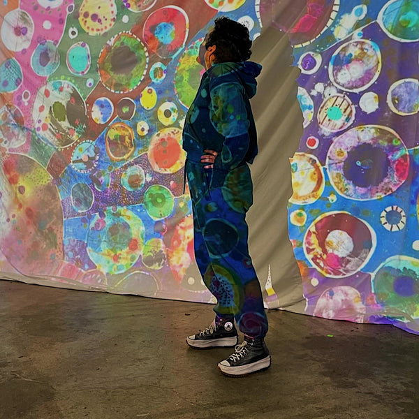 Artist Liz Tran, on set, standing in front of a projection of her artwork