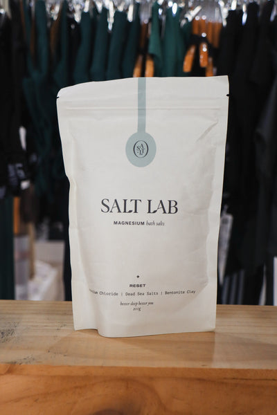 A bag of Salt Lab's Magnesium Bath Salts in front of green activewear