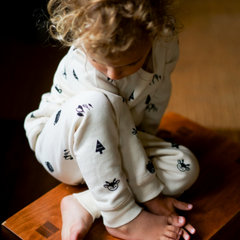 Toddler sitting on stool wearing a cotton fleece pajama set in natural with black forest print 