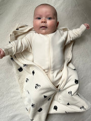 Baby in natural colored footie pajama and sleep sack that is unzipped to show footie