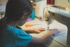 Little girl sitting at sewing machine with back to camera 