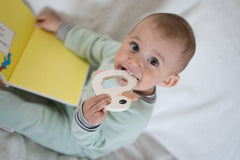 baby sitting up and looking into camera wearing a mint footie and holding a book