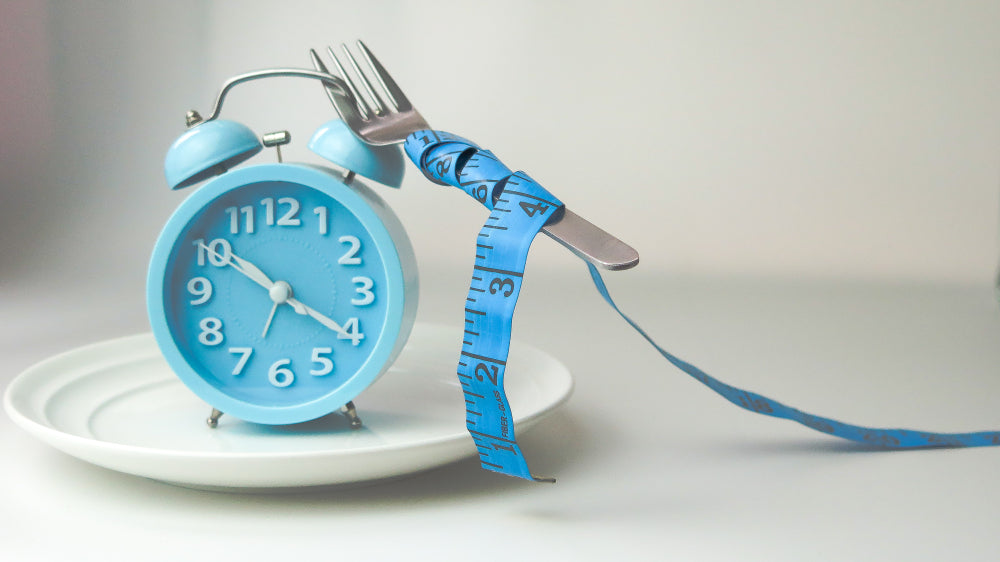 clock and fork with measuring tape on white plate ,diet, weight loss, intermittent fasting concept