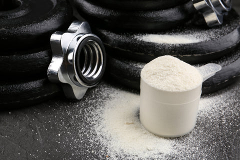 Measuring scoop of protein powder and weight plates on grey table,