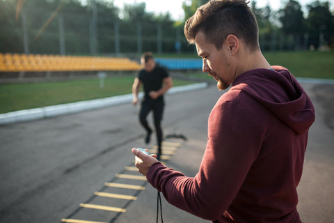 personal trainer with stopwatch measuring emom of male client exercising outdoors