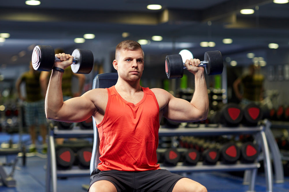 muscular guy doing seated dumbbell shoulder press in gym